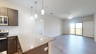 This thoughtfully designed 2-bedroom, 2-bathroom residence offers a functional and modern single-floor layout. The open-concept kitchen and living area serves as the heart of the home, where light wood-look flooring flows seamlessly throughout. The kitchen is well-equipped with stainless steel appliances — including a refrigerator, range, microwave, and dishwasher — complemented by rich dark cabinetry, a classic subway tile backsplash, and granite countertops that extend to a breakfast bar with pendant lighting overhead. The living area opens directly to a private balcony through a sliding glass door, allowing natural light to fill the space. Both bedrooms feature plush carpet, ceiling fans, and windows with outdoor views. Each bedroom is served by a dedicated bathroom finished with granite-topped dark vanities, wood-look tile flooring, and tiled tub-shower combinations. Both bedrooms also include walk-in closets with built-in shelving and hanging rods, providing generous storage. A separate laundry closet with shelving adds further practicality. Clean white walls, consistent finishes, and a neutral palette throughout lend the space a bright, cohesive, and move-in-ready appeal.