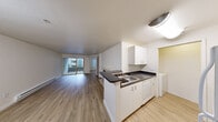 Located at 600 7th Ave in the heart of Seattle, this one-bedroom, two-bathroom residence offers a practical and well-appointed single-floor layout. The open-concept kitchen and living area forms the core of the unit, where light wood-style flooring runs throughout. The kitchen features white cabinetry, dark countertops, a stainless steel sink, and a dishwasher, arranged along a peninsula that separates it from the living space. The living room is highlighted by a fireplace with a classic surround and a sliding glass door that opens onto a private balcony, bringing in natural light. Baseboard heating is present throughout the unit. The bedroom is carpeted and includes a ceiling fan, a window with blinds that allows natural light, and a closet with mirrored sliding doors. An adjacent vanity area with a sink and mirror connects conveniently to the bathroom, which includes a full soaking tub with a shower. A dedicated in-unit laundry room provides side-by-side washer and dryer hookups with additional shelving. Clean white walls and a neutral palette lend a bright, move-in-ready feel throughout this efficiently designed Seattle residence.