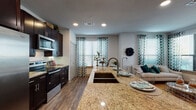 This single-floor residence offers a thoughtfully designed open-concept layout that seamlessly connects the kitchen, dining, and living areas. The kitchen is a standout, featuring dark espresso cabinetry, a full suite of stainless steel appliances, a subway tile backsplash, and a large granite-topped island with an undermount sink and bar seating — ideal for both cooking and casual dining. Wood-look flooring flows throughout the main living area, adding warmth and continuity.

The living room is bright and welcoming, with multiple windows dressed in decorative patterned curtains and fitted blinds, allowing ample natural light. A glass panel door provides additional brightness and potential outdoor access.

The bedrooms are comfortably sized, each featuring plush carpeting and generous closet space with built-in shelving and hanging rods. One bedroom is highlighted by a ceiling fan and a tufted upholstered headboard wall, while another showcases a more intimate, softly lit atmosphere.

The bathrooms are well-finished, with dark or navy cabinetry, granite countertops, undermount sinks, and large mirrors. One bathroom includes a full soaking tub with tiled surround and a shower curtain enclosure, while another features a hallway-style layout connecting directly to a bedroom. Throughout, the space maintains a cohesive, modern residential aesthetic.