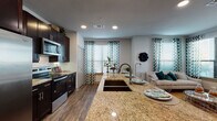 This single-floor residence offers a thoughtfully designed open-concept layout that seamlessly connects the kitchen, dining, and living areas. The kitchen is a standout, featuring dark espresso cabinetry, a full suite of stainless steel appliances, a subway tile backsplash, and a large granite-topped island with an undermount sink and bar seating — ideal for both cooking and casual dining. Wood-look flooring flows throughout the main living area, adding warmth and continuity.

The living room is bright and welcoming, with multiple windows dressed in decorative patterned curtains and fitted blinds, allowing ample natural light. A glass panel door provides additional brightness and potential outdoor access.

The bedrooms are comfortably sized, each featuring plush carpeting and generous closet space with built-in shelving and hanging rods. One bedroom is highlighted by a ceiling fan and a tufted upholstered headboard wall, while another showcases a more intimate, softly lit atmosphere.

The bathrooms are well-finished, with dark or navy cabinetry, granite countertops, undermount sinks, and large mirrors. One bathroom includes a full soaking tub with tiled surround and a shower curtain enclosure, while another features a hallway-style layout connecting directly to a bedroom. Throughout, the space maintains a cohesive, modern residential aesthetic.