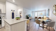This well-designed single-floor residence offers a clean, contemporary aesthetic throughout, characterized by light wood-style flooring, crisp white walls, and an abundance of natural light. The open-concept layout seamlessly connects the kitchen, dining, and living areas, creating a cohesive and functional living space. The kitchen is a standout feature, showcasing white shaker-style cabinetry, a classic subway tile backsplash, stainless steel appliances, and a generous island with seating — ideal for both meal prep and casual dining. The living area is bright and welcoming, anchored by large windows with horizontal blinds that allow ample natural light while offering privacy. The bedroom is a serene retreat, featuring light wood flooring, large windows with outdoor views, and warm, neutral tones. A second bedroom or flex room provides additional versatility. The bathroom is finished with a floating vanity, undermount sink, quartz-style countertop, and a large mirror, reflecting a modern and streamlined design sensibility. Throughout the residence, the consistent use of light tones, natural textures, and thoughtful detailing contributes to an overall ambiance that is calm, airy, and inviting.