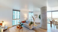 This thoughtfully designed single-floor high-rise residence offers a bright, open-concept layout bathed in natural light from expansive floor-to-ceiling windows. The living area is a standout space, anchored by a striking exposed concrete cylindrical column that adds an industrial-chic contrast to the warm light wood flooring and crisp white walls. Multiple large windows frame sweeping panoramic views of the surrounding cityscape and distant mountains, creating an airy, elevated atmosphere throughout.

The kitchen is sleek and modern, featuring flat-front cabinetry in a soft blue-grey tone, white quartz countertops, a chevron-patterned tile backsplash with under-cabinet lighting, and stainless steel appliances including a gas range and built-in microwave. The layout flows seamlessly into the dining and living areas, ideal for both everyday living and entertaining.

The bedroom is generously proportioned, offering floor-to-ceiling windows with breathtaking elevated city views, light wood flooring, and a built-in closet. The full bathroom features large-format tile flooring, a soaking tub with shower, and a dark-toned vanity with clean, minimalist finishes.

A well-organized hallway with louvered double closet doors connects the living spaces, completing this polished and contemporary residence.