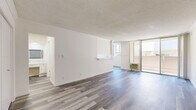 Located at 8441 Balboa Blvd in the Northridge neighborhood of Los Angeles, this well-appointed unit offers a clean, modern aesthetic across a thoughtfully organized single-floor layout. The bright living room serves as the heart of the space, featuring wide-plank wood-look flooring, crisp white walls, a textured ceiling, and a wall-unit air conditioner. Large floor-to-ceiling sliding glass doors open directly onto a private balcony, flooding the interior with natural light and providing outdoor views of the surrounding neighborhood. A pass-through counter connects the living area to the galley-style kitchen, which is outfitted with white cabinetry, marble-look countertops, a full suite of white appliances including a range and refrigerator, and ample upper and lower cabinet storage. The bedroom offers generous closet space and natural light through a window with views of mature palm trees. A dedicated dressing area with marble-look countertops and built-in cabinetry leads to the primary bathroom, which impresses with full marble-look tile flooring, a sleek floating vanity, and a shower-tub combination. A second bathroom provides additional convenience. Consistent wood-look flooring and a neutral color palette tie the entire space together with a cohesive, contemporary feel.
