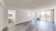 Located at 8441 Balboa Blvd in the Northridge neighborhood of Los Angeles, this well-appointed unit offers a clean, modern aesthetic across a thoughtfully organized single-floor layout. The bright living room serves as the heart of the space, featuring wide-plank wood-look flooring, crisp white walls, a textured ceiling, and a wall-unit air conditioner. Large floor-to-ceiling sliding glass doors open directly onto a private balcony, flooding the interior with natural light and providing outdoor views of the surrounding neighborhood. A pass-through counter connects the living area to the galley-style kitchen, which is outfitted with white cabinetry, marble-look countertops, a full suite of white appliances including a range and refrigerator, and ample upper and lower cabinet storage. The bedroom offers generous closet space and natural light through a window with views of mature palm trees. A dedicated dressing area with marble-look countertops and built-in cabinetry leads to the primary bathroom, which impresses with full marble-look tile flooring, a sleek floating vanity, and a shower-tub combination. A second bathroom provides additional convenience. Consistent wood-look flooring and a neutral color palette tie the entire space together with a cohesive, contemporary feel.