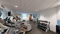 Located at 331 Justison Street in Wilmington, Delaware, this fitness center offers a thoughtfully designed exercise space that accommodates a wide variety of workout routines. The room features a clean, modern aesthetic with white walls, a drop-tile ceiling with recessed lighting, and durable rubber flooring throughout — all contributing to a functional and professional gym environment.

The cardio section is well-appointed with multiple treadmills and elliptical machines, including Precor and Life Fitness models, each equipped with individual display screens for an engaging workout experience. A large wall-mounted mirror expands the visual depth of the space and enhances the sense of openness. The strength training area includes a multi-station cable machine, a rack of free weights ranging in various sizes, medicine balls, stability balls, and exercise mats, providing ample options for resistance and functional training.

Natural light filters in through a window on one wall, complementing the overhead recessed lighting to keep the space bright and inviting. A water cooler station ensures hydration is always within reach. The layout is efficiently organized to allow users to move freely between equipment, making the most of the available floor space. Overall, this fitness center delivers a comprehensive and well-maintained facility for residents or guests seeking a convenient place to exercise.