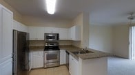 This single-floor residence offers a clean, functional layout designed for comfortable everyday living. The kitchen is a standout feature, showcasing white shaker-style cabinetry that extends to the upper walls, providing ample storage space. Granite countertops in warm, earthy tones add a touch of elegance and durability to the workspace. The kitchen is equipped with a full suite of stainless steel appliances, including an electric range, over-the-range microwave, and dishwasher, all contributing to a cohesive, modern aesthetic. A peninsula counter with an integrated sink extends into the space, creating a natural division between the kitchen and adjoining areas while offering additional prep and seating potential. Light tile flooring runs throughout the kitchen, lending a bright and easy-to-maintain surface underfoot. Overhead, a flush-mounted ceiling light fixture provides consistent illumination across the workspace. The neutral color palette of soft white and warm beige walls creates a welcoming ambiance that complements the overall design. The open sightlines and efficient use of space make this a highly practical and inviting single-floor home.
