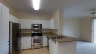 This single-floor residence offers a clean, functional layout designed for comfortable everyday living. The kitchen is a standout feature, showcasing white shaker-style cabinetry that extends to the upper walls, providing ample storage space. Granite countertops in warm, earthy tones add a touch of elegance and durability to the workspace. The kitchen is equipped with a full suite of stainless steel appliances, including an electric range, over-the-range microwave, and dishwasher, all contributing to a cohesive, modern aesthetic. A peninsula counter with an integrated sink extends into the space, creating a natural division between the kitchen and adjoining areas while offering additional prep and seating potential. Light tile flooring runs throughout the kitchen, lending a bright and easy-to-maintain surface underfoot. Overhead, a flush-mounted ceiling light fixture provides consistent illumination across the workspace. The neutral color palette of soft white and warm beige walls creates a welcoming ambiance that complements the overall design. The open sightlines and efficient use of space make this a highly practical and inviting single-floor home.
