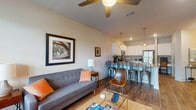 This single-floor residence offers a cohesive, open-concept design that efficiently connects its key living areas. The entryway leads into a corridor that opens to the main living and kitchen spaces, with wood-style flooring extending throughout the common areas for a clean, unified aesthetic.

The living room is well-proportioned, featuring a ceiling fan, a private entrance door with transom window, and ample natural light from multiple windows fitted with horizontal blinds. A wall-mounted television and built-in shelving unit anchor one side of the room, while the opposite side accommodates comfortable seating, creating a functional and inviting atmosphere.

The kitchen is outfitted with white shaker-style cabinetry, granite countertops, stainless steel appliances including a range, microwave, and refrigerator, and a peninsula with bar seating illuminated by pendant lighting. This space transitions seamlessly into the dining and living areas.

The bedroom offers plush carpeting, a ceiling fan, and a natural-light-filled window with exterior views. A dedicated closet provides ample storage. The adjoining bathroom features granite countertops, white cabinetry, an undermount sink, and marble-style tile flooring, with direct access to the bedroom for added convenience.