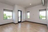 This single-floor unit offers a thoughtfully designed open layout with a clean, contemporary aesthetic throughout. Light hardwood flooring runs continuously across all areas, complemented by neutral-toned walls, dark baseboards, and recessed lighting that collectively create a bright and cohesive interior.

The main living area is generously proportioned, featuring soaring ceilings and multiple windows that flood the space with natural light. A glass-paned door opens directly onto a private balcony, offering elevated views of the surrounding neighborhood and tree canopy.

The kitchen is well-appointed with stainless steel appliances, including a refrigerator, electric range, microwave, and dishwasher. Light wood upper cabinetry with open shelving pairs with darker lower cabinets and crisp white countertops, creating a functional and visually balanced cooking space.

An additional open area, with exposed industrial ductwork overhead and a built-in work surface, adds flexible use potential — suited for a studio, office, or creative workspace. This area also benefits from recessed lighting and high ceilings, reinforcing the loft-inspired character.

The bathroom is well-sized and features a glass-enclosed walk-in shower, a wall-mounted vanity with a white countertop, a large mirror, and a wide window that introduces natural light and treetop views, enhancing the sense of openness throughout.