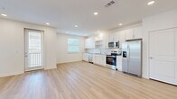 This well-designed single-floor residence offers a clean, contemporary aesthetic defined by a bright and open layout. The heart of the home is a spacious open-concept living and kitchen area, where light hardwood-style flooring flows seamlessly underfoot. The kitchen is outfitted with crisp white shaker cabinetry, granite countertops, a white subway tile backsplash, and a full suite of stainless steel appliances, including a refrigerator, range, microwave, and dishwasher. Recessed lighting illuminates the space, while multiple windows dressed with blinds allow natural light to fill the room.

The bedroom features soft wall-to-wall carpeting, creating a comfortable contrast to the hardwood-style flooring found elsewhere. A walk-in closet with wire shelving and a hanging rod provides generous storage capacity. The bathroom is appointed with a white vanity featuring a granite countertop, wood-look tile flooring, and connects conveniently to the bedroom via an en-suite layout. A ceiling fan in the adjoining space adds to the home's functionality. Throughout the residence, white walls, clean lines, and consistent finishes contribute to a cohesive, modern atmosphere that is both practical and inviting.