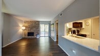 This single-floor residence offers a thoughtfully designed open-concept layout highlighted by rich, dark hardwood flooring that flows seamlessly throughout the space. The expansive living room serves as the centerpiece, anchored by a striking full-height brick accent wall with a built-in fireplace. A large sliding glass door fills the room with natural light and provides direct access to a private balcony with outdoor views, creating an inviting and airy atmosphere.

Adjacent to the living area, the kitchen is both functional and stylish, featuring crisp white cabinetry, quartz countertops with a marble-like finish, a stone tile backsplash, and black appliances including a range, microwave, dishwasher, and refrigerator. A breakfast bar connects the kitchen to the living space, enhancing the open flow of the floor plan.

The bedrooms are generously sized, each equipped with ceiling fans and continued hardwood flooring. The primary bedroom benefits from its own sliding door access to a balcony, along with a dedicated walk-in closet. The bathroom is clean and modern, offering a quartz vanity, tub-shower combination, and updated fixtures. A hallway with a built-in desk nook adds a practical touch to this well-rounded residence.