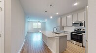 This single-floor residence features a thoughtfully designed open-concept layout that seamlessly connects the kitchen and living areas. The kitchen serves as the focal point, centered around a large island with a granite countertop, an undermount sink, and pendant lighting overhead. Grey cabinetry extends to the ceiling, providing generous storage, while a full suite of stainless steel appliances — including a refrigerator, range, and built-in microwave — completes the space. Light wood-tone flooring runs throughout the main living area, enhancing the bright, airy atmosphere created by recessed lighting and a ceiling fan.

The living area extends to a windowed wall, allowing natural light to fill the space. Bedrooms are carpeted for comfort and include ceiling fans and windows with outdoor views. At least one bedroom features a walk-in closet with built-in shelving. The bathroom is finished with a granite vanity, grey cabinetry with chrome hardware, a tiled tub-shower combination, and light wood-tone flooring consistent with the rest of the unit. Throughout, the neutral color palette and modern finishes contribute to a clean, contemporary aesthetic.