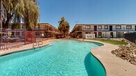 Located at 4235 N 35th Ave in Phoenix, Arizona, this multi-unit residential property offers a compelling blend of Southwest architectural style and functional outdoor amenities. The single-story building features a neutral stucco exterior with dark trim accents, flat rooflines, and individual unit entrances framed by iron-barred windows — design elements characteristic of the region's building tradition.

The centerpiece of the property is a generously sized, freeform swimming pool situated within a central courtyard. The pool's curvilinear shape and clear turquoise water create an inviting focal point, complemented by a surrounding concrete deck ideal for lounging. Adjacent to the pool, a well-maintained stretch of lush green artificial turf provides additional outdoor recreational space, offering a cool contrast to the desert environment.

The courtyard is enclosed by a sturdy wrought iron perimeter fence, ensuring both security and an open, airy feel. Desert-appropriate rock landscaping lines portions of the property, minimizing water usage while maintaining a clean, polished appearance. Mature palm trees and shade trees punctuate the skyline, adding vertical interest and a quintessential Arizona ambiance. The property basks in the abundant natural sunlight characteristic of the Phoenix climate, making the outdoor spaces especially appealing year-round.