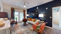 This thoughtfully designed single-floor residence in Holly Springs, NC, showcases a cohesive blend of bold color choices and modern finishes throughout its well-appointed layout. The open-concept kitchen and dining area serves as the heart of the home, anchored by a substantial granite-topped island with a built-in sink and seating for multiple bar stools. White shaker cabinetry, subway tile backsplash, and a full suite of stainless steel appliances — including a range, microwave, refrigerator, and dishwasher — complete the kitchen's polished, functional design. Hardwood-style flooring flows through the main living areas, contrasting elegantly with the striking deep navy accent wall that defines both the kitchen-dining space and the living room. The living room features French doors that invite natural light and outdoor views, complemented by a ceiling fan and vibrant, eclectic décor. The bedrooms offer plush carpeting and natural light from well-placed windows, with one bedroom featuring a rich forest-green accent wall. Two bathrooms provide granite vanities; one includes a glass-enclosed walk-in shower, while the other offers a tub-shower combination — both finished with clean, contemporary fixtures and ample storage.