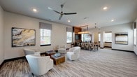 This single-floor communal space is thoughtfully designed to accommodate a variety of activities, blending comfort and functionality in a cohesive, contemporary aesthetic. The interior is finished in warm neutral tones throughout, with patterned low-pile carpeting underfoot and recessed lighting complemented by ceiling fans that contribute to an open, airy atmosphere.

The lounge area serves as the heart of the space, furnished with plush white swivel chairs arranged around rustic wooden coffee tables, creating an inviting setting for relaxed conversation or quiet reading. Multiple windows dressed with gray roman shades allow generous natural light to filter in, while curated abstract artwork adds visual interest to the walls.

Transitioning seamlessly from the lounge, the dining area features a substantial wooden table surrounded by upholstered chairs, anchored by a warm-toned wood entertainment wall housing a flat-screen television. An industrial-style rectangular chandelier with candle-like bulbs hangs overhead, adding a refined focal point.

The business center offers two dedicated workstations, each equipped with a desktop computer and L-shaped wood desk, paired with tufted cognac leather chairs. A multifunction printer is also available, ensuring practical productivity needs are fully met within the space.
