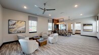 This single-floor communal space is thoughtfully designed to accommodate a variety of activities, blending comfort and functionality in a cohesive, contemporary aesthetic. The interior is finished in warm neutral tones throughout, with patterned low-pile carpeting underfoot and recessed lighting complemented by ceiling fans that contribute to an open, airy atmosphere.

The lounge area serves as the heart of the space, furnished with plush white swivel chairs arranged around rustic wooden coffee tables, creating an inviting setting for relaxed conversation or quiet reading. Multiple windows dressed with gray roman shades allow generous natural light to filter in, while curated abstract artwork adds visual interest to the walls.

Transitioning seamlessly from the lounge, the dining area features a substantial wooden table surrounded by upholstered chairs, anchored by a warm-toned wood entertainment wall housing a flat-screen television. An industrial-style rectangular chandelier with candle-like bulbs hangs overhead, adding a refined focal point.

The business center offers two dedicated workstations, each equipped with a desktop computer and L-shaped wood desk, paired with tufted cognac leather chairs. A multifunction printer is also available, ensuring practical productivity needs are fully met within the space.