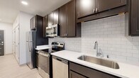 This thoughtfully designed one-bedroom, one-bathroom unit in De Forest, Wisconsin, offers a compact yet functional layout across a single floor. The open-concept living and kitchen area is anchored by light-toned hardwood-style flooring that extends throughout the main space, creating a clean and cohesive aesthetic. The kitchen is a standout feature, showcasing rich dark espresso cabinetry, white subway tile backsplash, crisp white countertops, and a full suite of stainless steel appliances including a range, microwave, and dishwasher. A peninsula provides additional prep and dining space. The living area benefits from abundant natural light through a large window and sliding glass door that opens onto a private balcony, offering pleasant outdoor views of the surrounding landscape. A ceiling fan adds comfort to the space. The bedroom features soft wall-to-wall carpeting and a ceiling fan, providing a cozy and quiet retreat. The bathroom continues the design language of the unit with matching dark cabinetry, white countertops, light hardwood-style flooring, a glass-enclosed shower, and built-in open shelving for convenient storage. The unit also includes an electrical panel accessible from the main living area, reflecting practical, move-in-ready functionality throughout.