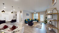 This single-floor residence offers a thoughtfully designed open-concept layout that seamlessly connects the living, dining, and kitchen areas. The living room is a vibrant and inviting space, highlighted by light hardwood-style flooring, a ceiling fan, and large windows dressed with bold yellow curtains that allow generous natural light to fill the room. A glass-paneled exterior door provides additional brightness and outdoor views.

The kitchen is well-equipped and functional, featuring rich dark cabinetry with modern hardware, white countertops, stainless steel appliances including an electric range and built-in microwave, and under-cabinet lighting that adds a warm ambiance. The adjacent dining area accommodates a round glass-top table with contemporary white chairs, making it an ideal space for casual meals.

The primary bedroom offers a comfortable retreat with plush carpeting, a ceiling fan, and a large window that brings in ample natural light. A second bedroom, also carpeted and ceiling fan-equipped, provides flexible use as a guest room or additional sleeping space.

The bathroom is clean and modern, appointed with dark cabinetry matching the kitchen, a white countertop vanity, a glass-enclosed walk-in shower, and light hardwood-style flooring. Together, these spaces create a cohesive, comfortable, and stylishly appointed home.