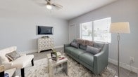This single-floor unit offers a cohesive, contemporary design unified by herringbone-patterned tile flooring and a soft, neutral color palette of whites and cool grays. The living room is a welcoming space, highlighted by a large window with horizontal blinds that allows generous natural light to fill the room. A ceiling fan adds functional comfort, while the open layout accommodates a living and dining area that flows seamlessly into the kitchen. The kitchen is well-equipped, featuring granite countertops with a speckled finish, light wood cabinetry, a stainless steel undermount sink, and a stylish mosaic tile backsplash in shades of white and gray. The bedroom is generously proportioned, offering dual sliding-door closets for ample storage, a ceiling fan, and a wall-mounted air conditioning unit. A large window brings in natural light, enhancing the room's airy feel. The bathroom is clean and functional, featuring a full-size bathtub with a shower combination, white subway tile surround, and a window above the tub for added brightness. Throughout the unit, consistent flooring, clean white walls, and thoughtful design details create a polished and comfortable living environment.