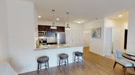 This single-floor residence is designed with an open, functional layout that promotes a comfortable flow between living spaces. The kitchen serves as a central feature, outfitted with dark espresso cabinetry contrasted by a light granite countertop, a white subway tile backsplash, and stainless steel appliances including a refrigerator, range, and microwave. A peninsula with seating for three, illuminated by a pair of brushed nickel pendant lights, connects the kitchen to the main living area. Recessed lighting and wood-look flooring carry throughout the kitchen and entry areas.

The living room is bright and welcoming, featuring sliding glass doors that allow natural light and provide access to an outdoor area. Wood-look flooring continues here, complementing the neutral wall tones.

The bedroom is a comfortable retreat with plush carpeting, a large window, and access to a well-organized closet. An in-unit washer and dryer are conveniently accessible from the bedroom area.

The bathroom is finished with marble-style tile flooring, a granite-topped dark vanity, and a full tub and shower combination. Clean white walls and brushed nickel fixtures contribute to the space's polished, contemporary aesthetic throughout.