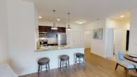 This single-floor residence is designed with an open, functional layout that promotes a comfortable flow between living spaces. The kitchen serves as a central feature, outfitted with dark espresso cabinetry contrasted by a light granite countertop, a white subway tile backsplash, and stainless steel appliances including a refrigerator, range, and microwave. A peninsula with seating for three, illuminated by a pair of brushed nickel pendant lights, connects the kitchen to the main living area. Recessed lighting and wood-look flooring carry throughout the kitchen and entry areas.

The living room is bright and welcoming, featuring sliding glass doors that allow natural light and provide access to an outdoor area. Wood-look flooring continues here, complementing the neutral wall tones.

The bedroom is a comfortable retreat with plush carpeting, a large window, and access to a well-organized closet. An in-unit washer and dryer are conveniently accessible from the bedroom area.

The bathroom is finished with marble-style tile flooring, a granite-topped dark vanity, and a full tub and shower combination. Clean white walls and brushed nickel fixtures contribute to the space's polished, contemporary aesthetic throughout.