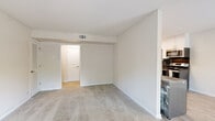 This single-floor residence offers a thoughtfully designed layout with a clean, neutral color palette that creates a bright and welcoming atmosphere. The open living area is finished with plush wall-to-wall carpeting and features multiple windows dressed with horizontal blinds, allowing natural light to fill the space while offering views of surrounding greenery. Ceiling fans in the bedrooms provide both comfort and airflow, while the soft, neutral wall tones lend a calm and versatile backdrop throughout.

The kitchen stands out as a clear highlight of the home, showcasing a modern renovation with two-tone cabinetry — crisp white uppers paired with slate gray lowers — and a bold dark subway tile backsplash that adds striking contrast. Stainless steel appliances, including a refrigerator, range, and over-the-range microwave, complement the contemporary design. Light wood-style flooring runs through the kitchen and adjoining areas, and an in-unit washer is conveniently situated nearby.

The bedrooms are generously sized, each featuring soft carpeting, ceiling fans with integrated lighting, and windows that bring in natural light. The bathroom is finished with a white vanity topped with dark granite countertop, a round mirror, and tile flooring, offering a clean and modern aesthetic. Overall, the space presents a practical yet stylish living environment.