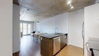 Located at 1140 Rue Wellington in Montréal's vibrant Griffintown neighbourhood, this one-bedroom, one-bathroom unit offers a thoughtfully designed layout that makes efficient use of its compact footprint. A defining architectural feature is the exposed concrete ceiling, which runs throughout the space, lending an industrial-chic character that contrasts beautifully with the crisp white walls and warm hardwood flooring.

The open-concept kitchen and living area form the heart of the unit. The kitchen is well-appointed with stainless steel appliances — including a refrigerator, electric range, and dishwasher — dark granite countertops, a dark tile backsplash, and sleek white upper cabinetry. A central island with an undermount sink doubles as a breakfast bar, enhancing both functionality and flow into the living area. Track lighting on the concrete ceiling illuminates the space effectively. Large sliding doors allow natural light to fill the living area.

The bedroom is a calm, light-filled retreat with hardwood flooring, a window with exterior views, and direct access to a dedicated closet. The bathroom is finished in neutral large-format tiles and features a deep soaker tub with an overhead shower, offering a clean and polished aesthetic. Overall, the unit presents a cohesive, modern industrial design throughout.