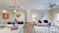 Located at 7880 Triangle Promenade Dr in Raleigh, NC, this 2-bedroom, 2-bathroom residence offers a thoughtfully designed single-floor layout that maximizes both comfort and functionality. The open-concept living, dining, and kitchen area serves as the heart of the home, where wood-style flooring flows seamlessly throughout. The kitchen features rich espresso-toned cabinetry, granite countertops, and black appliances, opening directly to a defined dining area adorned with wainscoting and crown molding details. The living room is bright and inviting, highlighted by a ceiling fan, crown molding, and a glass door that brings in natural light. The primary bedroom offers a comfortable retreat with plush carpeting, a bright window, and access to a generously sized walk-in closet complete with wire shelving systems for organized storage. The second bedroom provides additional flexibility. Both bathrooms are finished with wood-style flooring, vanities with ample counter space, and tub-shower combinations. A connecting hallway provides smooth flow between rooms, while two closets throughout the unit ensure practical storage. The neutral warm-gray color palette lends a calm, cohesive ambiance across the entire residence.