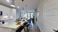 This single-floor residence showcases a thoughtfully designed open-concept layout that seamlessly connects the kitchen, dining, and living areas. The kitchen is a standout feature, outfitted with white shaker cabinetry extending to the ceiling, stainless steel appliances, under-cabinet lighting, and a central island with bar seating beneath stylish pendant lights. The countertops offer generous prep space, and the layout flows naturally toward the dining and living zones.

The living area is bright and welcoming, with French doors that invite natural light and provide views of the outdoors. A ceiling fan adds comfort, and the space is well-proportioned for both relaxing and entertaining. The bedroom is generously sized, featuring light wood-tone flooring, a ceiling fan, and a large window that draws in natural light.

The primary bathroom is finished with a dual-sink white vanity, dark hardware accents, marble-style tile flooring, and a soaking tub with subway tile surround. A second bathroom mirrors the refined aesthetic. Throughout the residence, light wood flooring, neutral tones, and clean-lined millwork create a cohesive, contemporary atmosphere that feels both functional and polished.