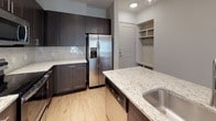 This well-appointed two-bedroom, two-bathroom residence is arranged on a single floor, offering a thoughtfully designed open-concept layout. The kitchen serves as a focal point, showcasing dark espresso cabinetry that extends to the ceiling, light granite countertops with subtle veining, and a tile backsplash. A central island with an undermount sink provides additional prep space and casual seating. Stainless steel appliances, including a French door refrigerator with ice and water dispenser, built-in microwave, and range, complete the space. Light wood-style flooring flows from the kitchen into the living area, which features a ceiling fan and access to an outdoor patio through a glass door, allowing natural light to fill the room. A built-in entry nook with open shelving offers convenient storage near the front door. Both bedrooms are finished with plush carpeting, ceiling fans, and windows that bring in natural light. Each bathroom is equipped with dark cabinetry, granite countertops, a framed mirror, and a tub-shower combination. One bathroom includes a walk-in closet, while additional closet storage is accessible throughout the unit.