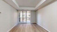 Located on the 11th floor at 140 Main St W in downtown Hamilton, this one-bedroom, two-bathroom condo offers a well-designed layout with contemporary finishes throughout. Light hardwood-style flooring flows seamlessly across the entire unit, complementing the neutral grey palette that creates a clean, modern aesthetic.

The open-concept kitchen is outfitted with rich dark-toned cabinetry, white countertops, a subway tile backsplash, and a full suite of stainless steel appliances including a refrigerator, electric range, microwave, and dishwasher. The kitchen opens directly to the combined dining and living area, which is bathed in natural light from large floor-to-ceiling windows and sliding glass doors that lead to the private balcony.

The spacious primary bedroom features a tray ceiling, generous proportions, and its own access to the outdoors through sliding glass doors. A dedicated den provides flexible space suitable for a home office or additional sleeping area. The unit includes two well-appointed bathrooms — one with a soaker tub and shower combination and a stone-topped vanity, and a second powder-style bathroom with a clean, minimalist design. In-suite laundry and a dedicated closet round out this efficiently planned urban residence.