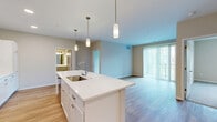 This thoughtfully designed 2-bedroom, 2-bathroom single-floor residence offers a comfortable and functional layout finished with modern details throughout. The open-concept kitchen and living area serves as the heart of the home, anchored by a large center island with a white quartz countertop, stainless steel sink, and stylish pendant lighting overhead. The kitchen is outfitted with tall white shaker-style cabinetry, stainless steel appliances including a range and built-in microwave, and light wood-tone flooring that carries through the living area. The living room is bright and airy, benefiting from a large sliding glass door fitted with vertical blinds that invites natural light and outdoor views. Both bedrooms are carpeted and generously sized, with one featuring a ceiling fan and a window overlooking greenery. Each bedroom is served by its own closet, including a walk-in closet with wire shelving. The two bathrooms are clean and functional — one features a full tub-shower combo, and the primary bath includes a white vanity with a mirror and light wood flooring. Neutral tones, clean lines, and consistent finishes create a cohesive and move-in-ready ambiance throughout the space.