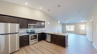 This single-floor home offers a thoughtfully designed open-concept layout that seamlessly connects the kitchen, dining, and living areas. The kitchen is a standout feature, showcasing rich dark cabinetry, granite countertops, a peninsula with a dual-basin sink, and a full suite of stainless steel appliances including a range, microwave, dishwasher, and refrigerator. Elegant pendant lighting and recessed fixtures illuminate the space, while soaring vaulted ceilings lend an impressive sense of openness and volume. Durable wood-look plank flooring runs throughout the main living areas, providing a warm and cohesive aesthetic. The living area benefits from natural light streaming through large windows that frame views of the surrounding outdoor greenery, with a ceiling fan adding comfort and character. The bedrooms are carpeted for comfort and feature ceiling fans, generous windows, and walk-in closets with built-in shelving. The primary suite connects directly to a well-appointed en-suite bathroom complete with dark cabinetry, granite countertops, and a walk-in closet with multi-tier shelving. The entry foyer welcomes visitors with natural light and direct views of the landscaped exterior. Throughout the home, neutral warm-toned walls and white trim create a clean, move-in-ready canvas.