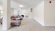 Located at 20142 53A Avenue in Langley, BC, this single-floor amenity space offers a clean, versatile layout well-suited for a variety of uses. The open-plan living room is finished with neutral-toned carpeting and crisp white walls, creating a bright and welcoming atmosphere throughout.

Large windows and a sliding glass door along one wall flood the space with natural light while offering views of the surrounding outdoor area, including a patio and the broader Langley streetscape. The generous proportions of the room allow for flexible furniture arrangements, and portable fabric room dividers are present, enabling the space to be sectioned off as needed for different activities or gatherings.

A structural column near the centre of the room adds an architectural element while subtly defining different zones within the open floor plan. Flush ceiling-mounted light fixtures provide consistent ambient lighting. A dedicated entrance door with a label and a secondary utility door are visible, along with an intercom panel, suggesting the space is part of a larger residential or mixed-use building. A separate area toward the back accommodates a table and chairs, ideal for meetings or dining. The overall ambiance is modern, minimal, and adaptable, making this a highly functional communal space.