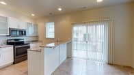 This three-floor property offers a well-designed interior with thoughtful finishes throughout. The kitchen is a standout feature, showcasing granite countertops with warm, varied toning atop a white beadboard peninsula that doubles as a breakfast bar. White cabinetry with glass-front upper panels provides both storage and visual openness, while recessed lighting illuminates the space evenly from above. Light-toned ceramic tile flooring runs throughout, contributing to a clean, cohesive aesthetic. A stainless steel sink is integrated into the peninsula, adding both functionality and a modern touch. Natural light is a defining characteristic of the kitchen, supplied generously through a window fitted with horizontal blinds and a wide sliding glass door dressed in vertical blinds. The sliding door leads to an outdoor area, providing a seamless indoor-outdoor connection. Neutral warm-toned walls complement the light fixtures and finishes, creating a bright and inviting atmosphere. The three-floor layout suggests ample living space distributed across multiple levels, offering flexibility for a variety of living arrangements. Overall, the property presents a clean, contemporary design with practical features and abundant natural light.