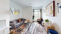 This thoughtfully laid-out one-bedroom, one-bathroom residence offers a cohesive modern design across its single floor. The open kitchen is a standout feature, equipped with stainless steel appliances, gray shaker-style cabinetry, white subway tile backsplash, and a generous white-topped island with bar seating — all illuminated by stylish pendant lighting and recessed ceiling lights. Light hardwood flooring flows throughout the main living areas, adding warmth and continuity.

The living room is bright and inviting, benefiting from a large window dressed with sheer curtains that frame outdoor views of the surrounding landscape. The space comfortably accommodates a full seating arrangement, making it ideal for both relaxing and entertaining.

The bedroom is carpeted for comfort and receives ample natural light through a wide window with outdoor views. It offers enough room for a full furniture arrangement and connects conveniently to the hallway.

The bathroom is clean and contemporary, featuring large-format tile flooring, a wood-toned vanity with a white countertop, a backlit rectangular mirror, and a tub-shower combination. A connecting hallway ties all rooms together efficiently, contributing to a practical and well-organized floor plan throughout.