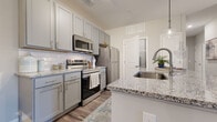 This single-floor residence in Columbus, Ohio offers a thoughtfully designed layout that maximizes functionality across its two bedrooms and one bathroom. The open-concept living area anchors the home, where the kitchen, dining, and living spaces flow seamlessly together. The kitchen is outfitted with gray shaker-style cabinetry, granite countertops, a subway tile backsplash, stainless steel appliances including a range, microwave, and refrigerator, and a central island with bar seating that doubles as a dining counter. Wood-look flooring runs throughout the main living areas, lending warmth and continuity to the space.

The adjacent dining area accommodates a round table and connects to the kitchen via a pass-through, while the living room features a glass-paneled exterior door that allows natural light to fill the space. Both bedrooms are carpeted and receive natural light through large windows with blinds. The primary bedroom offers a generous footprint with ample room for a full bedroom suite. The bathroom includes a glass-enclosed walk-in shower with white tile surround and wood-look flooring. A hallway connects the private and shared areas of the home, contributing to an efficient and comfortable floor plan.