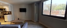 Located at 950 24th Street in the vibrant Georgetown neighborhood of Washington, DC, this single-floor residence offers a thoughtfully designed layout with modern finishes throughout. The living area features light wood-style flooring, neutral gray walls, and a large window that frames views of the surrounding neighborhood, flooding the space with natural light. A wall-mounted flat-screen TV and a relaxed seating arrangement make this an inviting area for everyday living. The kitchen is a standout feature, showcasing white flat-front cabinetry, crisp white countertops, and a bold slate-blue tile backsplash that adds a contemporary contrast. Stainless steel appliances — including a refrigerator, electric range, microwave, and dishwasher — provide a fully equipped and functional cooking space illuminated by recessed ceiling lighting. The bathroom is finished with full-surround rectangular tile work in warm neutral tones, complementing a soaking tub with an overhead shower, chrome fixtures, and clean white walls. The cohesive design language across all spaces — clean lines, light flooring, and a neutral palette — creates a calm, modern ambiance well-suited to the urban setting of Washington, DC.