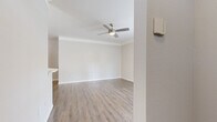 This single-floor residence offers a thoughtfully organized layout comprising a kitchen, living room, bedroom, bathroom, hallway, and entrance. The living room is a welcoming, open space finished with light wood-look luxury vinyl plank flooring, neutral gray walls, crown molding, and a ceiling fan with a light fixture. Large windows and French doors allow abundant natural light to fill the room, creating a bright and airy ambiance. The kitchen is well-appointed with white shaker-style cabinetry, a subway tile backsplash, light stone countertops, a peninsula with a sink, and a full suite of stainless steel appliances including a refrigerator, range, and over-the-range microwave. The bedroom is generously sized, featuring plush carpeting, a ceiling fan, a natural light window, and a double-door closet. The bathroom is clean and functional, outfitted with wood-look flooring, a tiled tub-shower combination, and standard fixtures. Throughout the home, a consistent neutral color palette and coordinated finishes contribute to a cohesive, modern aesthetic.