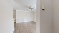 This single-floor residence offers a thoughtfully organized layout comprising a kitchen, living room, bedroom, bathroom, hallway, and entrance. The living room is a welcoming, open space finished with light wood-look luxury vinyl plank flooring, neutral gray walls, crown molding, and a ceiling fan with a light fixture. Large windows and French doors allow abundant natural light to fill the room, creating a bright and airy ambiance. The kitchen is well-appointed with white shaker-style cabinetry, a subway tile backsplash, light stone countertops, a peninsula with a sink, and a full suite of stainless steel appliances including a refrigerator, range, and over-the-range microwave. The bedroom is generously sized, featuring plush carpeting, a ceiling fan, a natural light window, and a double-door closet. The bathroom is clean and functional, outfitted with wood-look flooring, a tiled tub-shower combination, and standard fixtures. Throughout the home, a consistent neutral color palette and coordinated finishes contribute to a cohesive, modern aesthetic.