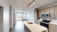 Located at 2920 Sixth Ave S in Birmingham, Alabama, this contemporary single-floor residence showcases a thoughtfully designed open-concept layout that seamlessly connects the kitchen, dining, and living areas. Rich hardwood-style flooring runs throughout the main living spaces, creating a warm and cohesive aesthetic.

The kitchen is a standout feature, equipped with stainless steel appliances including a refrigerator, range, and built-in microwave. Wood-toned cabinetry pairs with light quartz countertops and a mosaic tile backsplash, striking a balance between modern and approachable design. A central island with a deep undermount sink and a sleek pull-down faucet adds both functionality and a natural gathering point. Track lighting overhead ensures ample illumination throughout the space.

The living area extends toward floor-to-ceiling sliding glass doors that open onto a private balcony, offering views of the Birmingham skyline and filling the interior with generous natural light. A ceiling fan provides comfort throughout the open living zone.

The bedroom features plush carpeting, a ceiling fan, and a window with city views. The bathroom is finished with a dual-sink vanity, wood-toned cabinetry, and recessed lighting. A dedicated laundry area includes a stacked washer and dryer alongside open shelving for added storage convenience.