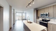 Located at 2920 Sixth Ave S in Birmingham, Alabama, this contemporary single-floor residence showcases a thoughtfully designed open-concept layout that seamlessly connects the kitchen, dining, and living areas. Rich hardwood-style flooring runs throughout the main living spaces, creating a warm and cohesive aesthetic.

The kitchen is a standout feature, equipped with stainless steel appliances including a refrigerator, range, and built-in microwave. Wood-toned cabinetry pairs with light quartz countertops and a mosaic tile backsplash, striking a balance between modern and approachable design. A central island with a deep undermount sink and a sleek pull-down faucet adds both functionality and a natural gathering point. Track lighting overhead ensures ample illumination throughout the space.

The living area extends toward floor-to-ceiling sliding glass doors that open onto a private balcony, offering views of the Birmingham skyline and filling the interior with generous natural light. A ceiling fan provides comfort throughout the open living zone.

The bedroom features plush carpeting, a ceiling fan, and a window with city views. The bathroom is finished with a dual-sink vanity, wood-toned cabinetry, and recessed lighting. A dedicated laundry area includes a stacked washer and dryer alongside open shelving for added storage convenience.