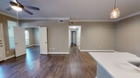 This thoughtfully designed 2-bedroom, 1-bathroom single-story home offers a cohesive and comfortable layout throughout. Dark hardwood-style flooring flows consistently across every room, complemented by crisp white crown molding and neutral warm-gray walls that create a clean, modern aesthetic.

The open-concept kitchen serves as a functional centerpiece, featuring white shaker cabinetry, stainless steel appliances, a decorative tile backsplash, pendant lighting, and a large island with white quartz countertops and a double sink — ideal for both cooking and casual dining. The kitchen opens directly into the living area, which is bathed in natural light from a front-facing door flanked by windows, and is equipped with a ceiling fan.

The spacious primary bedroom stands out with a distinctive curved bay window that floods the room with natural light, a ceiling fan, crown molding, and elegant double doors that open to a well-organized walk-in closet with built-in wire shelving systems. The en-suite bathroom features dual vanities with white quartz countertops, dual mirrors with lighted fixtures, a soaking tub, and a tiled shower enclosure.

The second bedroom offers generous proportions and matching finishes. Connecting hallways provide built-in shelving for additional storage, completing this well-designed home.