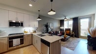 This single-floor residence presents a thoughtfully designed open-concept layout that seamlessly connects the kitchen, dining, and living areas. The kitchen is a standout feature, equipped with stainless steel appliances including a gas range, built-in microwave, and French door refrigerator. Two-toned cabinetry in light wood and soft white tones pairs with a granite-topped island that provides both additional workspace and seating for casual dining. A subway tile backsplash and pendant lighting complete the contemporary aesthetic.

The living area extends naturally from the kitchen, offering light wood-style flooring, a ceiling fan, and large windows dressed with dark draping curtains. A glass door opens to a private balcony, allowing natural light and outdoor views to enhance the space. The bedroom features a bold padded accent wall, ample natural light from a large window, and direct access to a well-appointed bathroom with a soaking tub and shower combination. An organized walk-in closet adjoins the bathroom for convenient storage.

A secondary bedroom offers comparable finishes and natural light. The entryway includes a functional mudroom-style area with a grid wall organizer and bench, alongside in-unit laundry access, contributing to a practical and cohesive living environment.