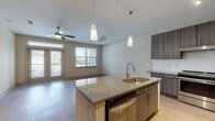 This single-floor, one-bedroom, one-bathroom unit offers a thoughtfully designed layout with contemporary finishes throughout. The open-concept kitchen serves as the centerpiece of the living space, showcasing dark wood-tone cabinetry with sleek hardware, granite countertops, and a classic white subway tile backsplash. A central island with a built-in sink, pendant lighting, and a dishwasher provides both functionality and a natural gathering point. Stainless steel appliances, including a refrigerator and range, complete the kitchen. Light wood-look flooring extends through the kitchen and living area, lending warmth and cohesion. The living room receives generous natural light through large windows and a set of French doors that open to a private outdoor area, with a ceiling fan adding comfort. The bedroom features soft carpeting and its own ceiling fan, creating a comfortable retreat. The bathroom is finished with granite countertops, dark cabinetry matching the kitchen, a tiled tub-shower combination, and light tile flooring. A walk-in closet adjacent to the bathroom provides ample storage, completing this well-balanced and modern living space.