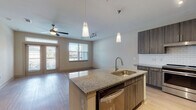 This single-floor, one-bedroom, one-bathroom unit offers a thoughtfully designed layout with contemporary finishes throughout. The open-concept kitchen serves as the centerpiece of the living space, showcasing dark wood-tone cabinetry with sleek hardware, granite countertops, and a classic white subway tile backsplash. A central island with a built-in sink, pendant lighting, and a dishwasher provides both functionality and a natural gathering point. Stainless steel appliances, including a refrigerator and range, complete the kitchen. Light wood-look flooring extends through the kitchen and living area, lending warmth and cohesion. The living room receives generous natural light through large windows and a set of French doors that open to a private outdoor area, with a ceiling fan adding comfort. The bedroom features soft carpeting and its own ceiling fan, creating a comfortable retreat. The bathroom is finished with granite countertops, dark cabinetry matching the kitchen, a tiled tub-shower combination, and light tile flooring. A walk-in closet adjacent to the bathroom provides ample storage, completing this well-balanced and modern living space.