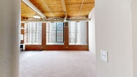 Located at 185 Pine St in Manchester, CT, this two-floor loft-style space showcases a compelling blend of industrial heritage and contemporary updates. The main living area immediately impresses with its soaring wooden beam ceilings, exposed brick accent walls, and expansive factory-style windows that flood the interior with natural light. A ceiling fan adds a functional touch to this airy, open area, which is finished with plush carpeting underfoot.

The kitchen is outfitted with crisp white shaker cabinetry, granite-look countertops, stainless steel appliances including a refrigerator and dishwasher, and wood-look flooring, offering a clean, modern aesthetic. The upper level continues the industrial loft character with timber beam ceilings, exposed brick, and large arched windows that provide striking views of the surrounding architecture.

Bedrooms are carpeted and well-proportioned, featuring spacious closets with classic bifold doors. Additional rooms maintain the brick-accented, light-filled character seen throughout. The bathroom is cleanly appointed with a white vanity, full tub-shower combo, and wood-look flooring. Soaring ceiling heights on the main floor, structural columns, and the warm contrast of brick against white walls give this space a distinctive, loft-inspired ambiance throughout both levels.
