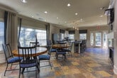 Located at 2090 Columns Dr in Cumming, GA, this single-floor space offers a thoughtfully designed interior that blends classic architectural details with contemporary finishes. Crown molding and recessed lighting are found throughout, contributing to a polished and cohesive aesthetic.

The kitchen is a standout area, showcasing white shaker-style cabinetry, dark granite countertops, and a neutral subway tile backsplash that extends to the ceiling. A central island with granite countertop and bar seating provides additional workspace, illuminated by a row of pendant lights overhead. Stainless steel appliances and a window above the sink allow natural light to brighten the space.

The dining area features rich slate tile flooring in warm, earthy tones, which flows seamlessly throughout the main living areas. Large windows dressed with layered linen drapes and blue patterned accents flood the room with natural light while offering views of the surrounding greenery. A round wood dining table with a chevron-pattern top serves as the focal centerpiece.

The living room, visible in the floorplan overview, includes a fireplace and wall-mounted television, offering a welcoming gathering space. An adjoining room with built-in shelving provides flexible use as a study or office. Overall, the space exudes a warm, inviting ambiance with refined design details throughout.