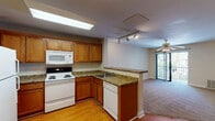 Located at 820 Macmillan Avenue in Wilmington, North Carolina, this single-floor residence offers a practical and comfortable layout designed for easy living. The kitchen serves as a central hub of the home, featuring warm honey-toned wood cabinetry, granite-look countertops, and a full suite of white appliances including a range with overhead microwave, dishwasher, and refrigerator. A skylight floods the kitchen with natural light, while a peninsula counter creates a seamless transition into the adjoining living area. The living space is finished with plush carpeting and is served by a ceiling fan, with a sliding glass door providing access to an outdoor area and drawing in additional natural light. Hardwood flooring runs throughout the kitchen and entry areas, adding warmth and continuity to the space. The bedroom is generously sized, featuring soft carpeting, a ceiling fan with light fixture, and dual windows that frame views of the surrounding greenery, creating a bright and airy atmosphere. The bathroom is finished with neutral tile flooring, warm beige walls, and a window that allows for natural ventilation. Clean white millwork and ample cabinetry throughout the home contribute to a cohesive, well-maintained interior aesthetic.