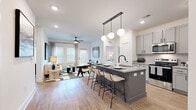 This well-appointed 2-bedroom, 2-bathroom residence is designed with a modern aesthetic and functional layout across a single floor. The open-concept living and dining area flows seamlessly into the kitchen, which serves as the heart of the home. The kitchen features gray shaker-style cabinetry, granite countertops, stainless steel appliances, and a large central island with pendant globe lighting overhead — ideal for both casual dining and entertaining. Light wood-style flooring runs throughout the main living areas, complementing the bright, white walls and recessed lighting. The living room benefits from natural light through large windows with blinds and includes a ceiling fan for added comfort. Both bedrooms offer plush carpeting and a calm, neutral palette. The primary bedroom connects to a well-sized en-suite bathroom featuring a double granite-top vanity, wood-look tile flooring, and a glass-enclosed walk-in shower. The second bathroom includes a soaking tub and granite vanity. Two dedicated closets provide generous storage, including a walk-in closet with multi-tier wire shelving. The overall ambiance is clean, contemporary, and cohesive throughout.